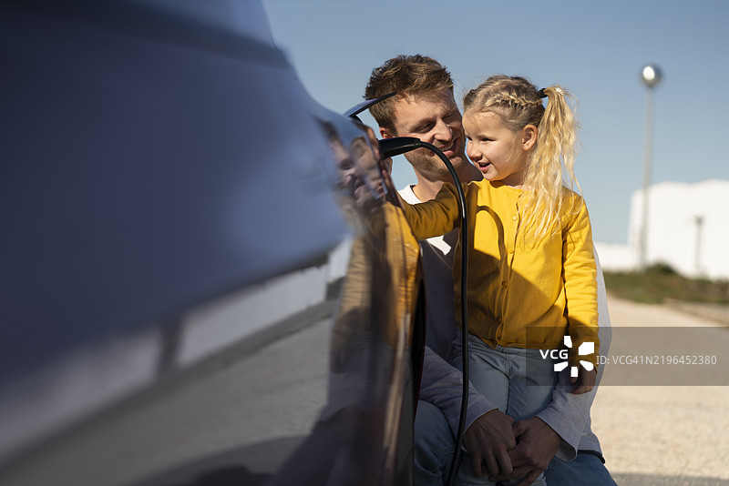 微笑的父亲与女儿一起为电动车充电图片素材