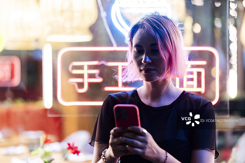 女人在发光的墙边使用智能手机图片素材