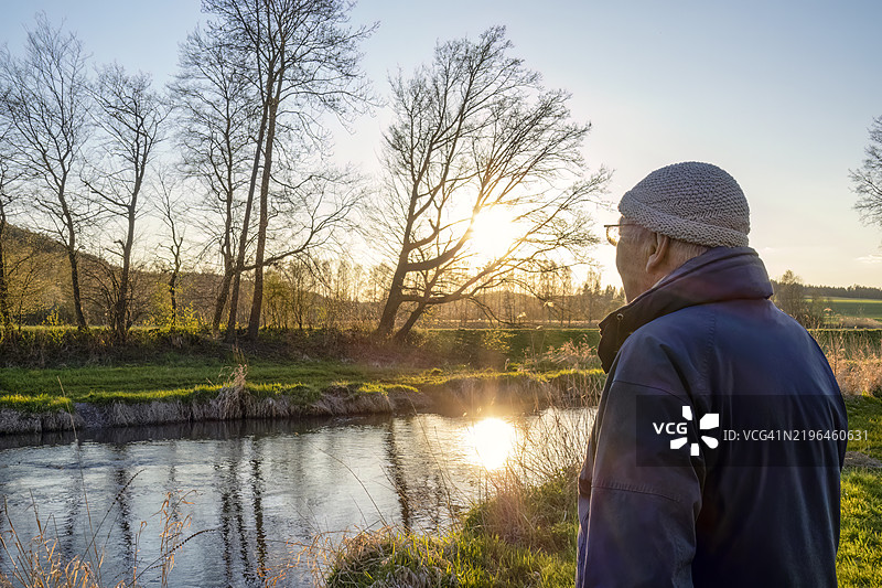 夕阳下，老年男子在河边欣赏风景图片素材