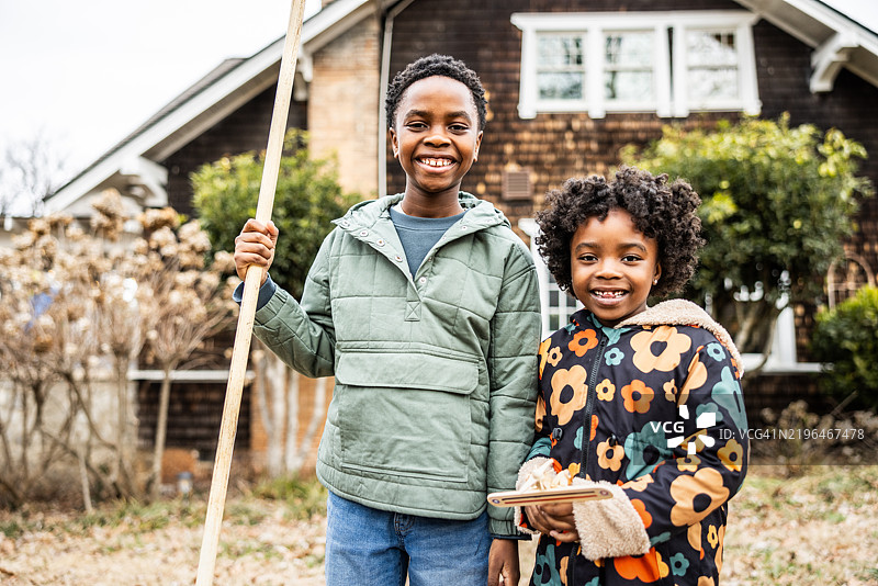 年轻的兄妹在郊区的院子里耙树叶图片素材