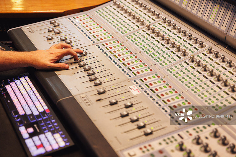 音响工程师/音乐制作人在录音室的混音台上工作的手部特写图片素材