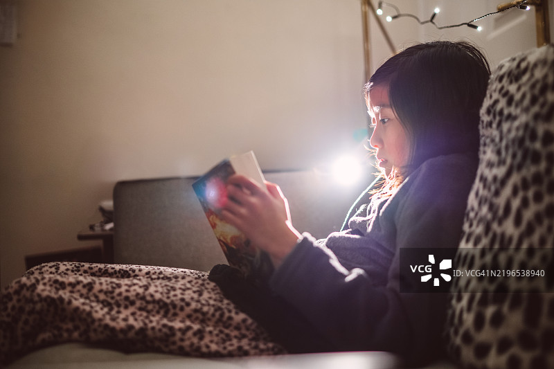 年轻女孩在家中柔和的灯光下沉浸于晚间阅读。图片素材