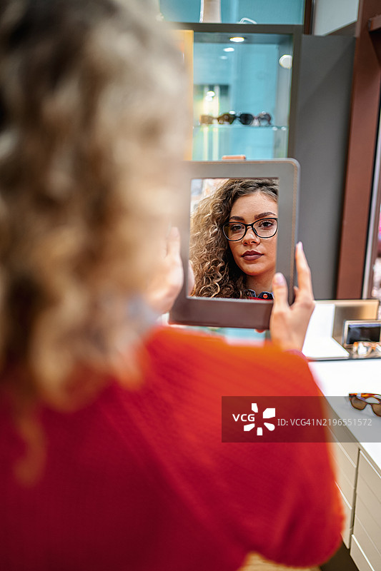 年轻女性在眼镜店试戴眼镜，照镜子。图片素材