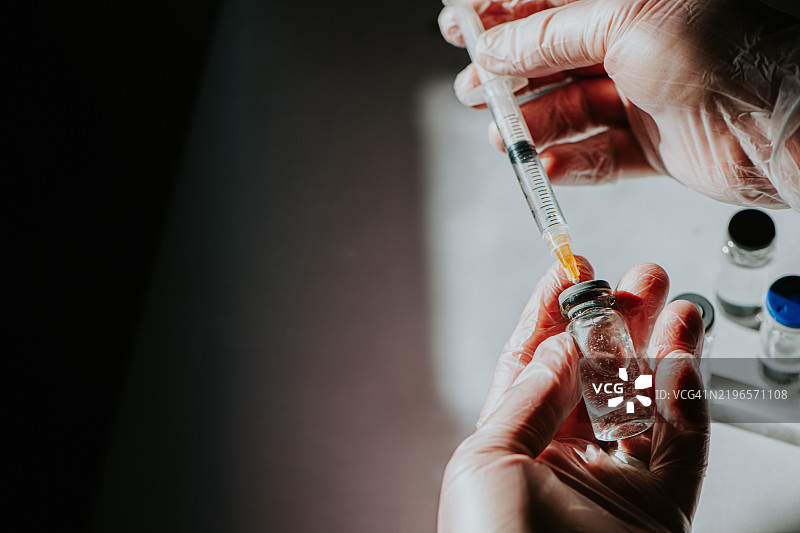 一名医疗专业人员使用注射器从药瓶中抽取液体药物。图片素材