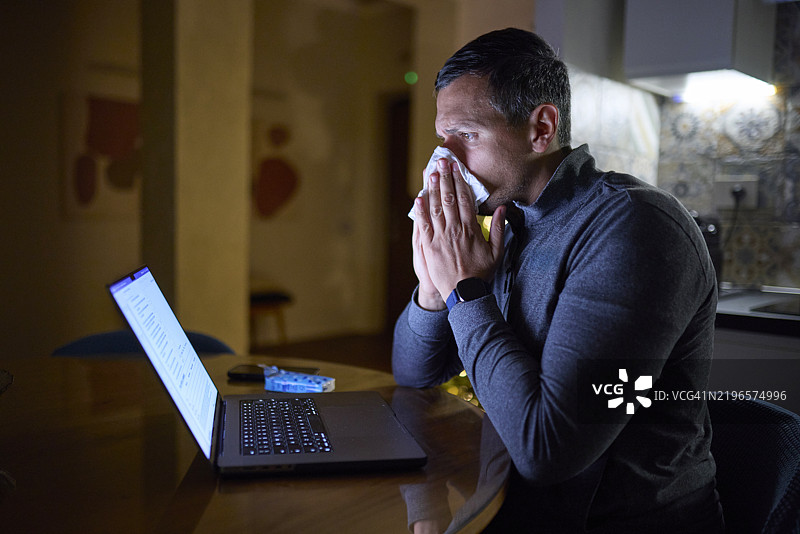 生病的男人在家里夜晚使用笔记本电脑图片素材