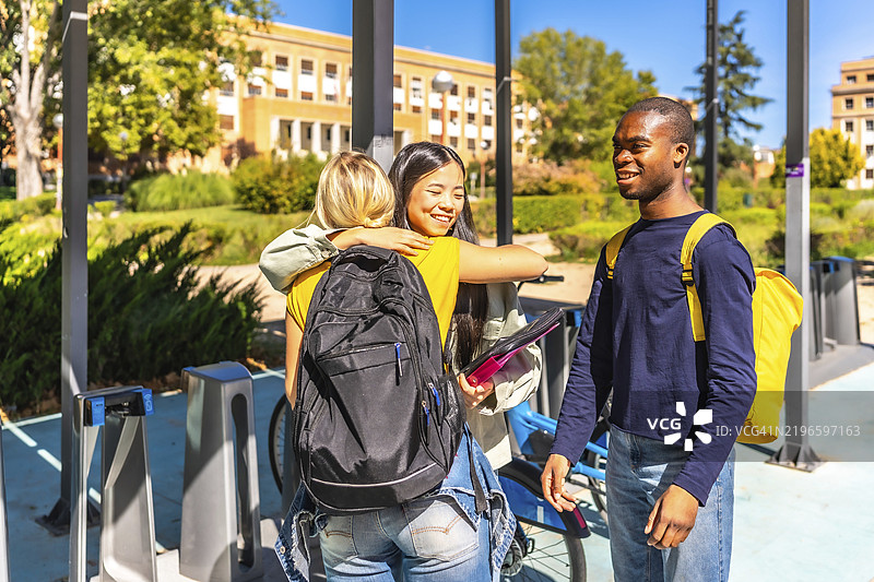 多民族的大学朋友在公共自行车租赁站旁拥抱告别图片素材