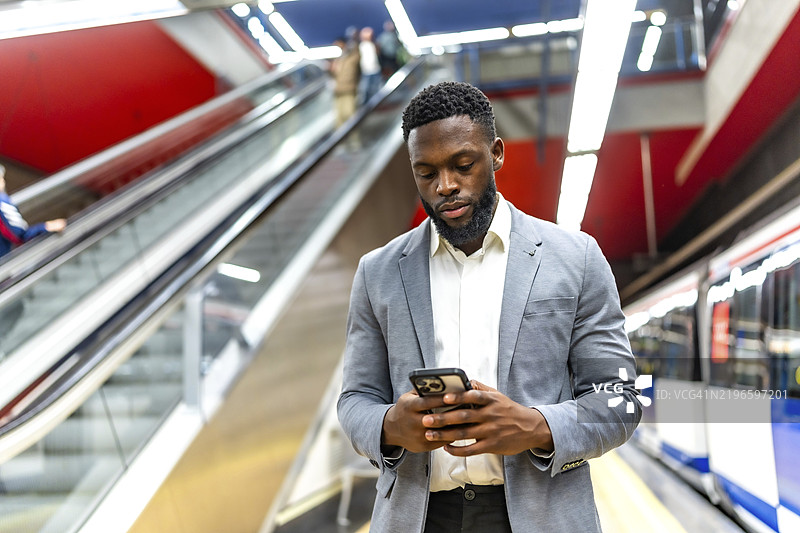 年轻商人在地铁站等车，使用智能手机查看信息，保持通勤时的联系。图片素材