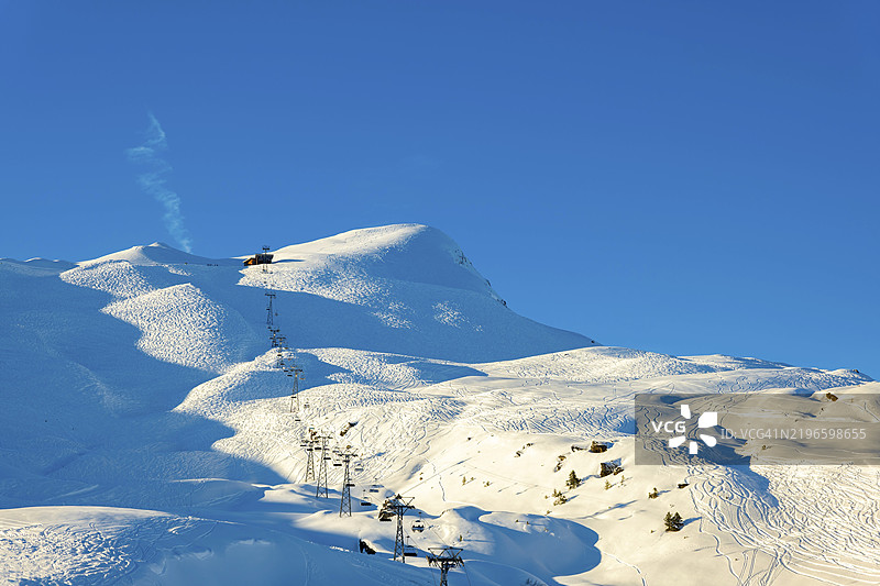 在瑞士伯尔尼州格林德瓦尔德的克莱因·谢德格，阳光明媚的冬日，蓝天清澈，海拔2000米的滑雪坡道上方有缆车，远处是山峰。图片素材