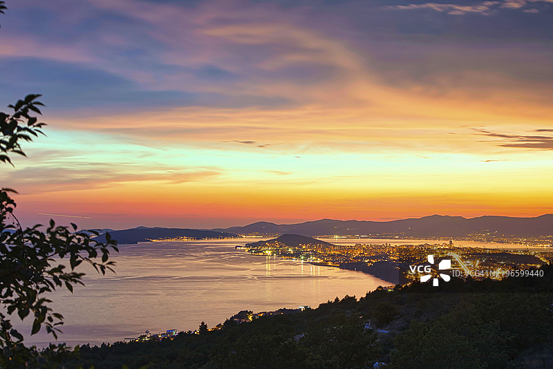 全景视角，城市灯光闪烁，五彩斑斓的日落映照在海面上，克罗地亚达尔马提亚的斯普利特。图片素材