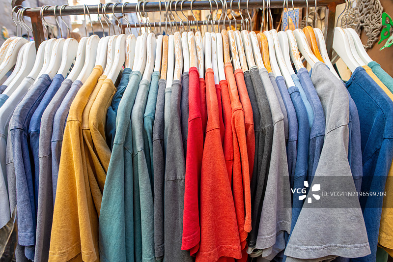 街道上的商店里，衣架上展示着许多色彩斑斓的T恤。图片素材