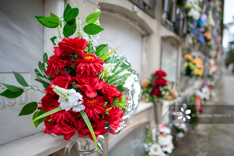 大型墓地的壁龛街道透视图，鲜花和其他祭品琳琅满目（特写人造花束）。图片素材