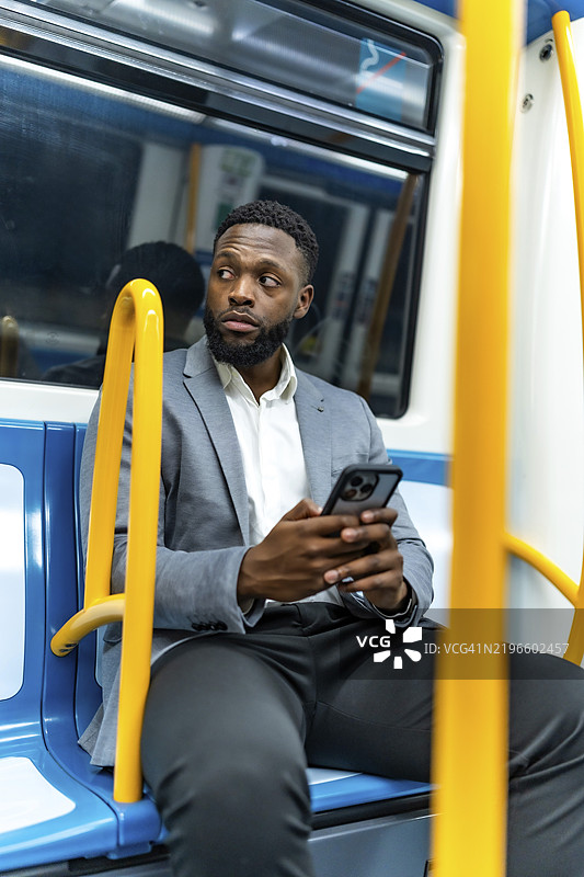 年轻商人在地铁上骑行，使用智能手机并侧目，沉浸在沟通和数字连接中图片素材