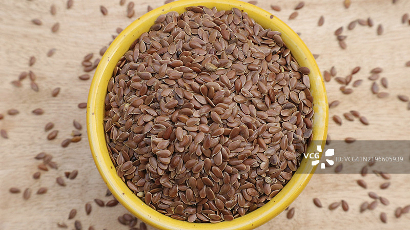 黄碗中的亚麻籽，周围散落着种子，背景为质朴的木材，俯视图图片素材