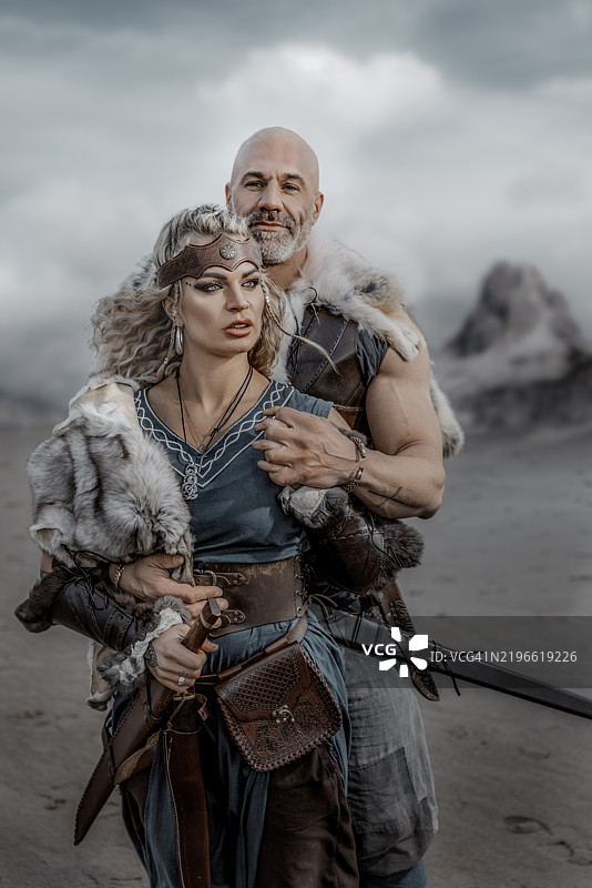一对美丽的维京战士情侣在海滩上，背景是山脉。图片素材