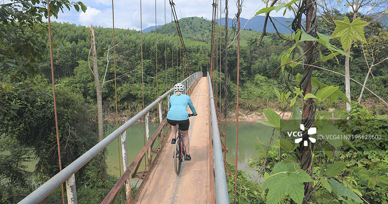 骑自行车的人在河上的悬索桥上骑行图片素材