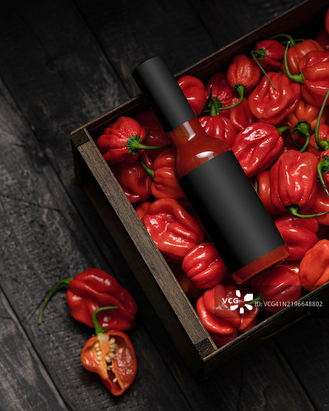 瓶装辣味哈瓦那辣椒酱放在木箱中，周围是许多红色哈瓦那辣椒。红辣椒酱。美味的食物。墨西哥烟熏辣椒。伯利兹热酱。墨西哥菜。辣味调味品。火辣的风味。留白空间。图片素材