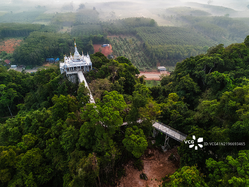 白色寺庙的鸟瞰图，坐落在郁郁葱葱的山上，通过悬空步道相连，四周环绕着雾气缭绕的森林和美丽的风景。图片素材