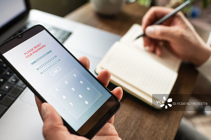手持智能手机和笔记本电脑的男子试图重置密码。数据安全、数据泄露和未经授权访问的概念。图片素材
