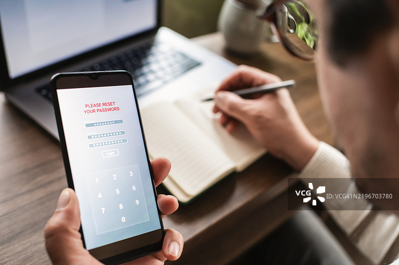 男子使用智能手机和笔记本电脑尝试重置密码。数据安全、数据泄露和未经授权访问的概念。图片素材