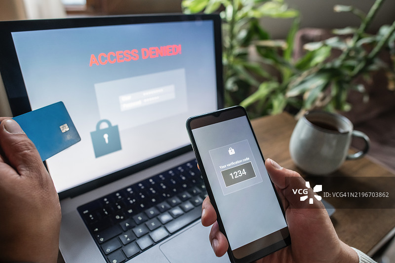 手持智能手机、笔记本电脑和信用卡的男子。双重身份验证、数据安全、数据泄露和未经授权访问的概念。图片素材
