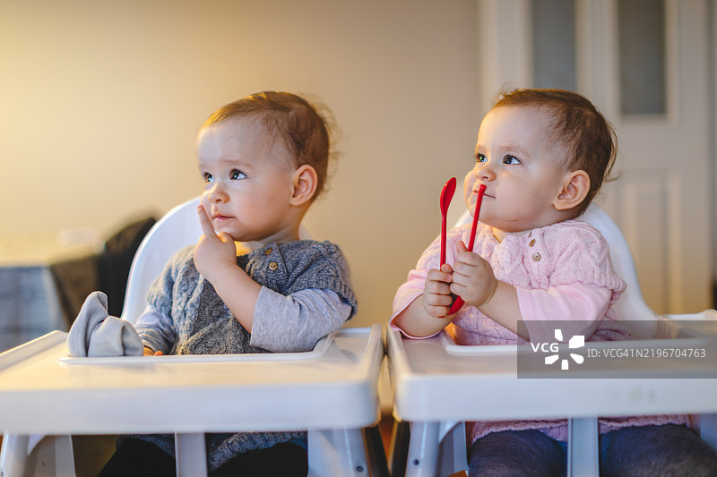 可爱的双胞胎宝宝坐在高脚椅上看卡通片图片素材