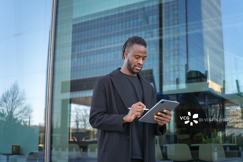 年轻商人在现代办公大楼前使用数字平板电脑图片素材