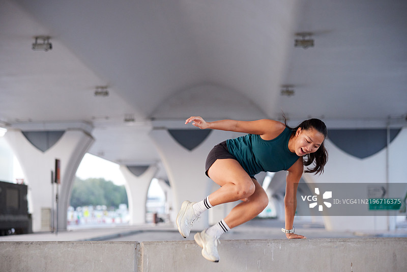 一位年轻女性在晨跑时跳过一个障碍。图片素材