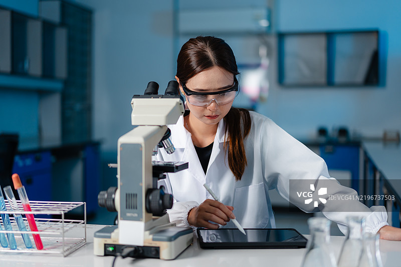 亚洲女性科学家在实验室使用显微镜进行科学研究图片素材