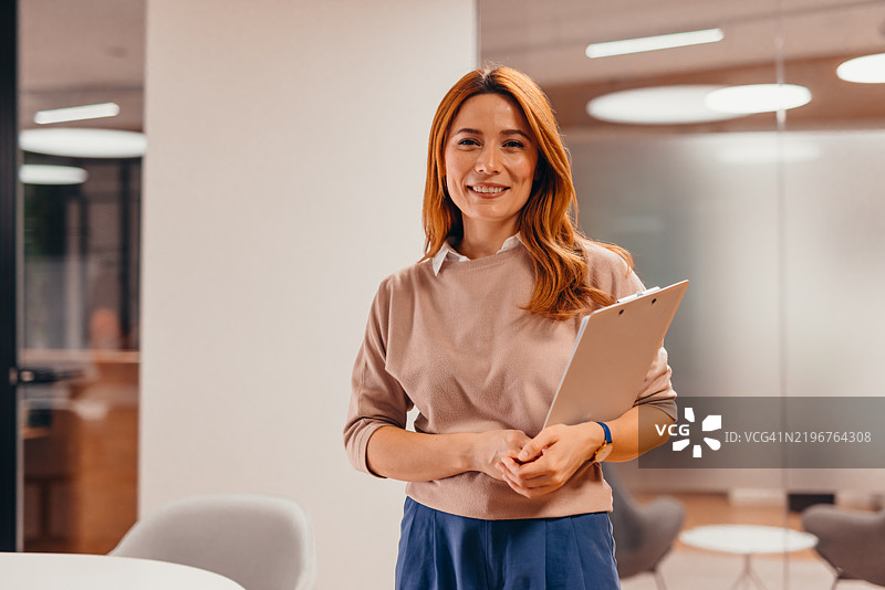 微笑的女商人在办公室里手持夹板图片素材