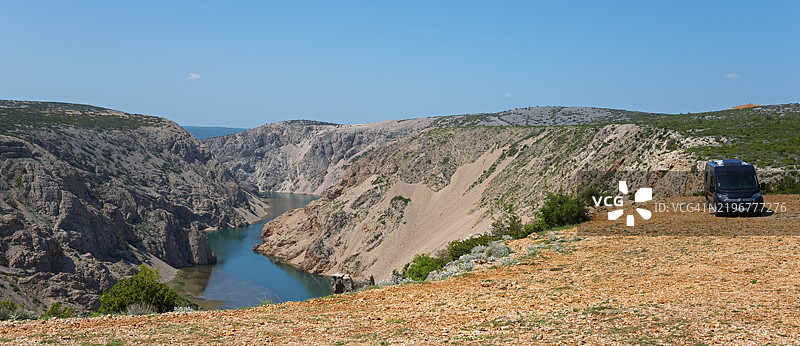 一辆房车停在岩石地形上,俯瞰着峡谷和河流,蓝天映衬下,位于克罗地亚扎达尔县的帕里热瓦茨卡·格拉维察,卡尔·梅电影的拍摄地点,兹尔曼尼亚河,雅塞尼采。图片素材