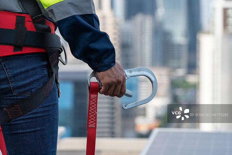 （安全身体施工）高空作业设备。用于工人的防坠落装置，带有安全身体安全带的钩子，聚焦选择。工人在施工背景中。图片素材