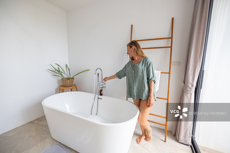 女性在现代浴室中测试水温图片素材