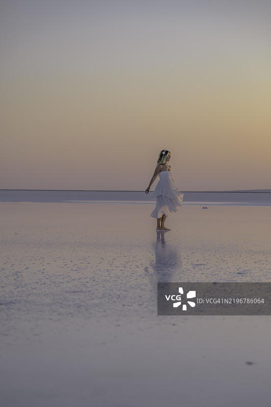 穿着白色连衣裙的年轻女性在土耳其阿克萨赖的图兹湖黄昏时分漫步图片素材