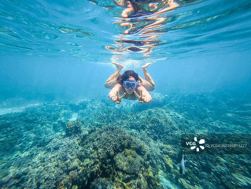 女性游泳者在坦桑尼亚桑给巴尔的五彩斑斓的珊瑚礁上浮潜，滑行在充满海洋生态系统的洁净碧绿水域中。图片素材