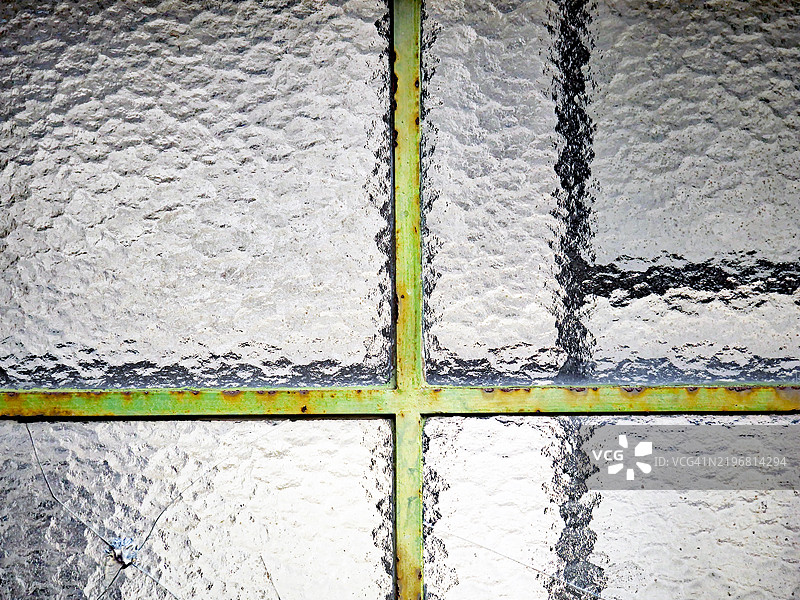 不透明且有纹理的窗户特写，配有涂漆和氧化的金属窗框。左下角的窗户因撞击而破损。图片素材