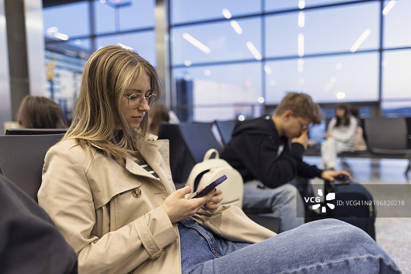 青少年在机场等待，使用他们的智能手机。图片素材