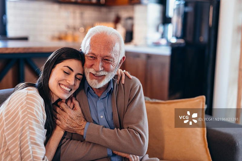 年轻女子在家沙发上拥抱微笑的老父亲图片素材
