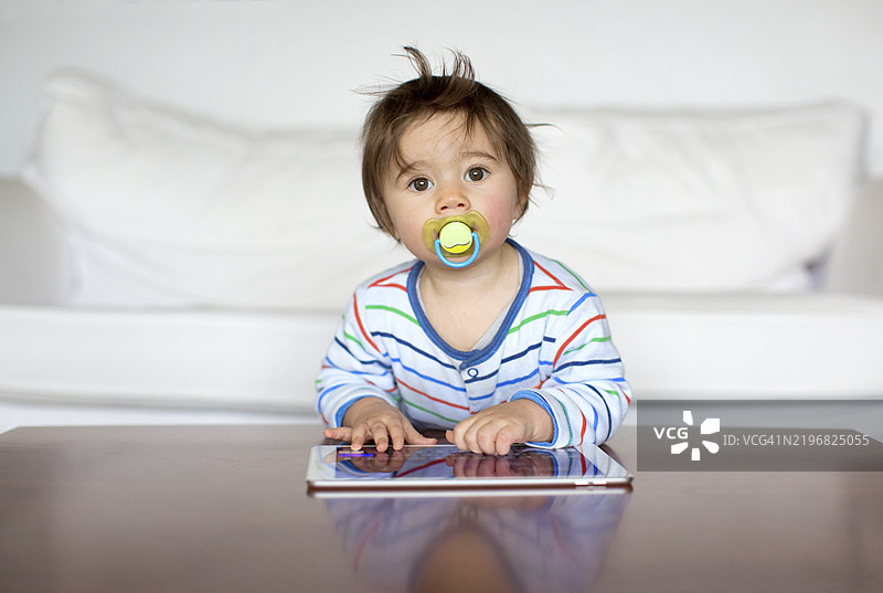好奇的幼儿在室内的木桌上探索平板电脑图片素材