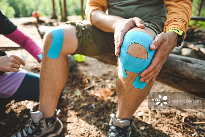 两名徒步旅行者在森林营地休息，处理轻微的伤口，周围环绕着大自然。图片素材