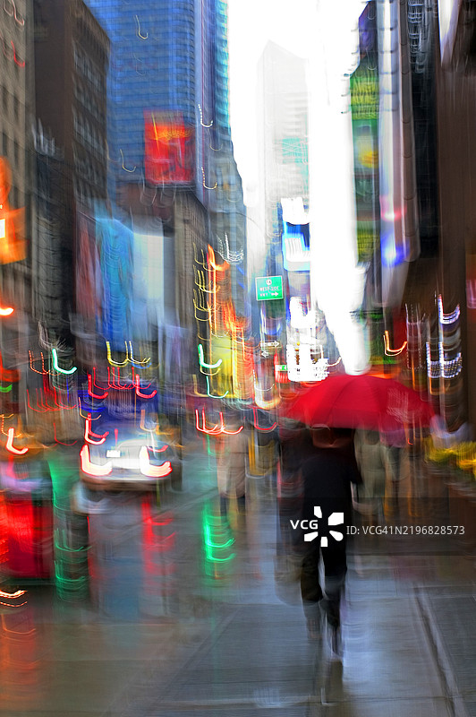 一张运动模糊的照片，展示了在雨中走在第七大道上、靠近时代广场的行人和雨伞，纽约市。图片素材