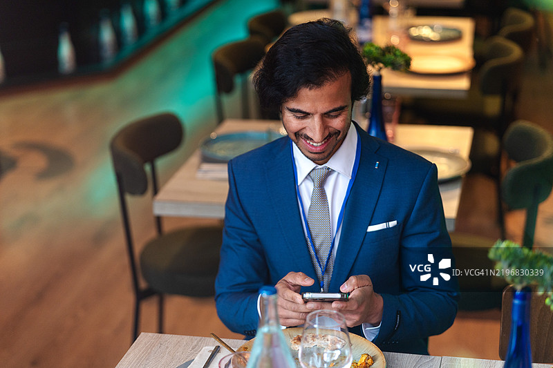 年轻的商人穿着西装和领带，在餐厅用餐时使用智能手机图片素材