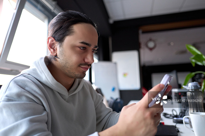 专注的年轻男性在现代办公室使用智能手机图片素材