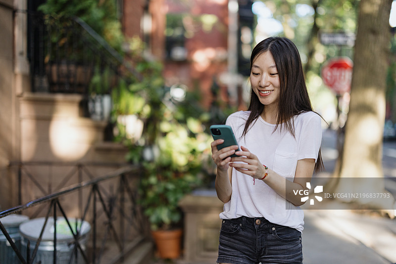 年轻女性在阳光明媚的户外微笑着使用智能手机图片素材