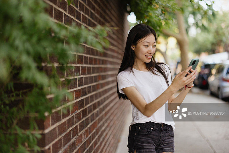 年轻女性在阳光明媚的户外与智能手机互动图片素材