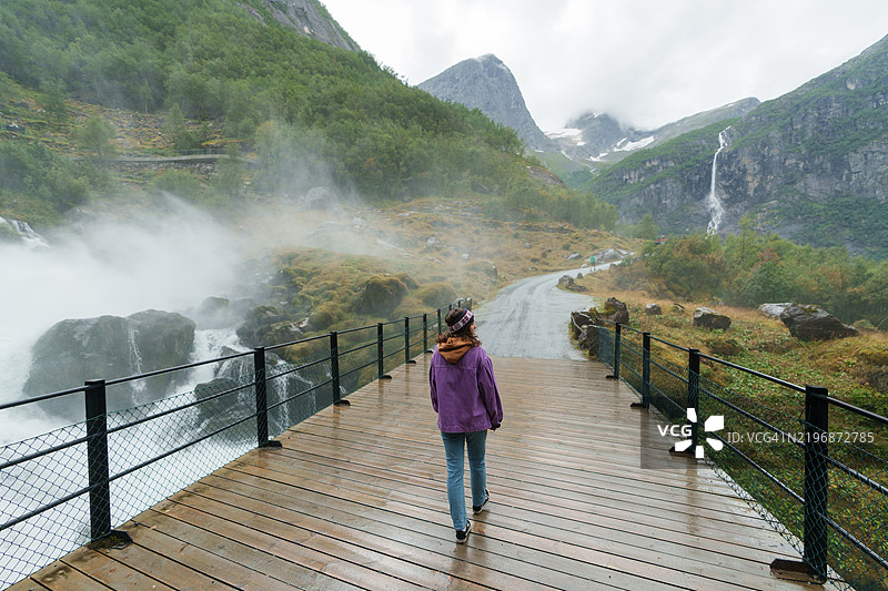 女人在挪威山中的壮观瀑布旁散步图片素材