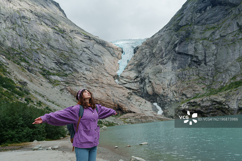 一位女性站在挪威的冰川旁，惊叹地欣赏风景。图片素材