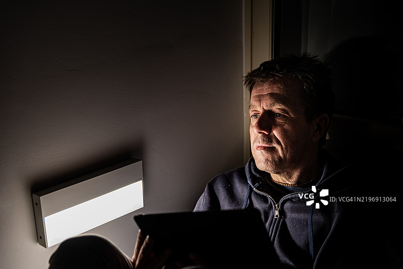 疲惫的成熟男性在夜晚坐在阳台上使用平板电脑图片素材