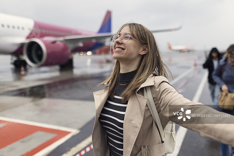 微笑的年轻女性从飞机上走下跑道，尽管天气阴雨，却依然充满快乐。图片素材
