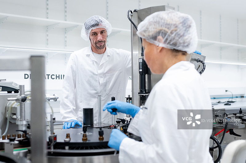 制药工人在灌装和包装瓶子的生产线上工作。图片素材