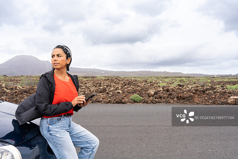 游客倚靠在她的车上，使用智能手机导航壮丽的火山景观，尽情享受冒险与探索。图片素材